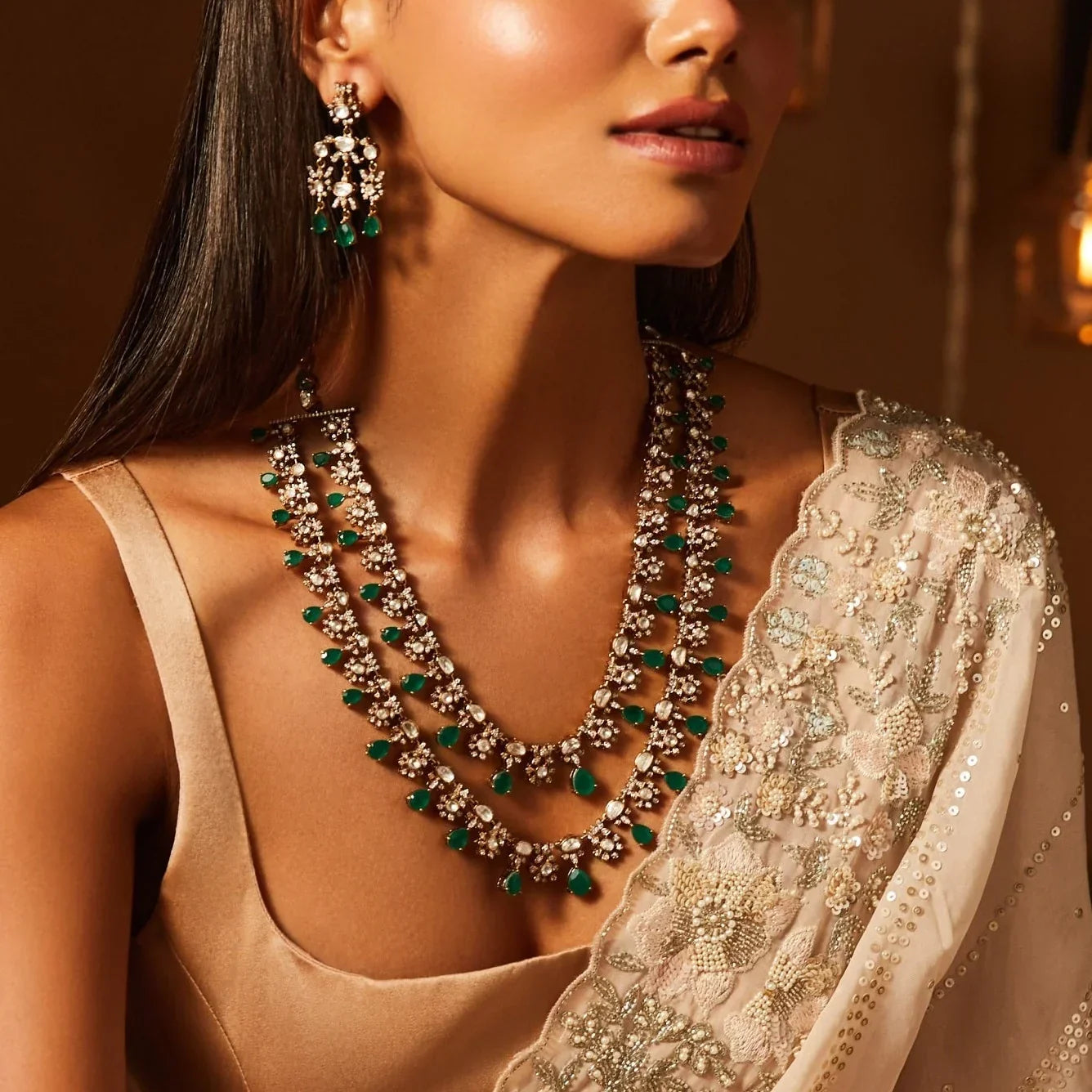 Woman wearing a layered silver necklace with green gemstones and matching statement earrings with a traditional embroidered outfit.
