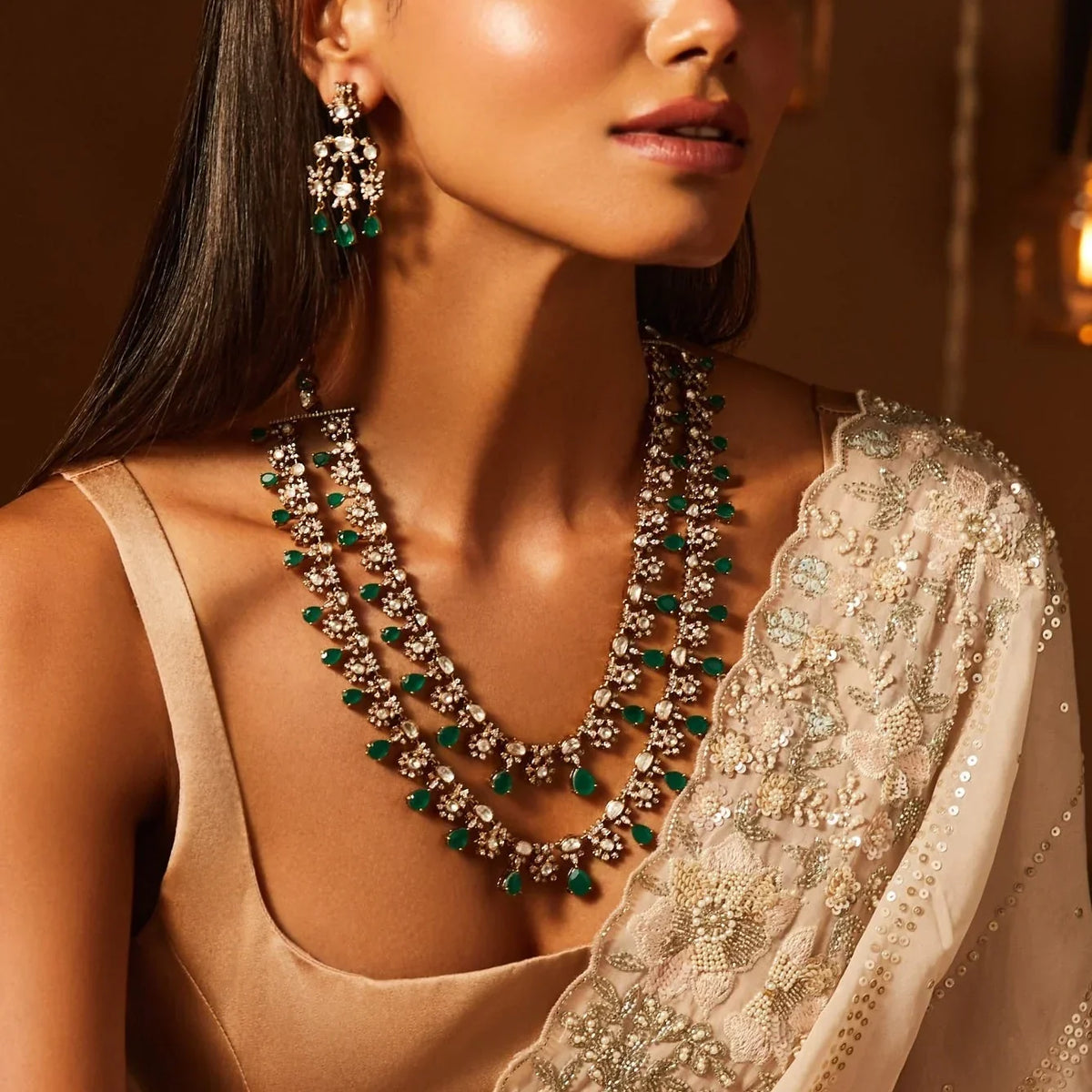 Woman wearing a layered silver necklace with green gemstones and matching statement earrings with a traditional embroidered outfit.
