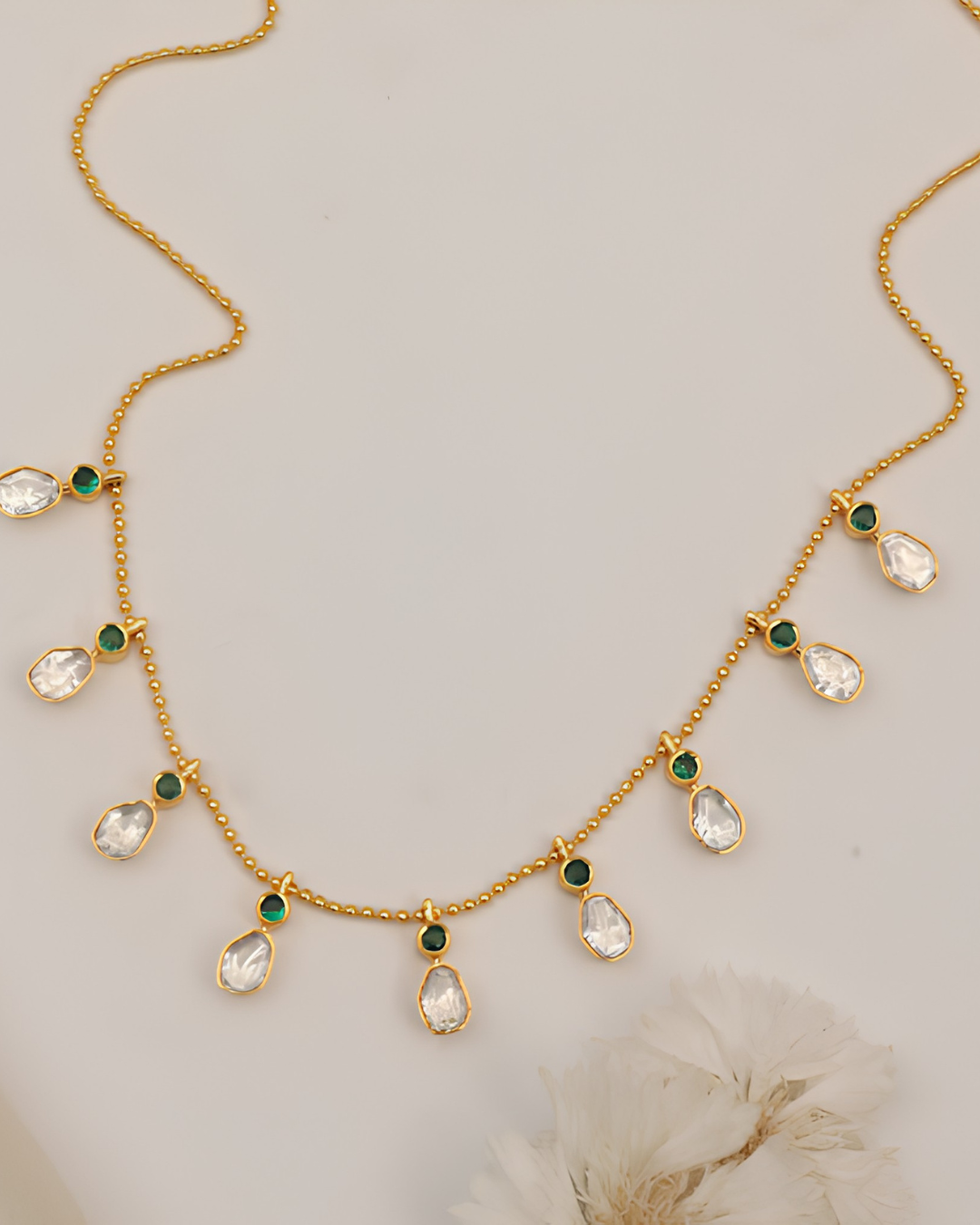 Elegant gold-toned necklace featuring green gemstone accents and sparkling teardrop crystal charms.