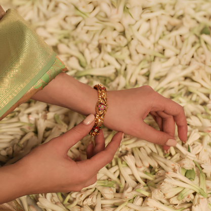 Close-up of a hand wearing an elegant gold bangle with red gemstones.