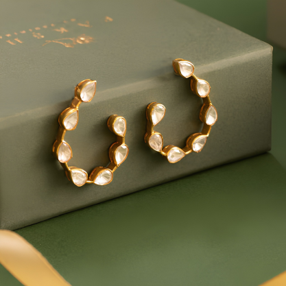 A pair of elegant gold-toned hoop earrings with oval white stones, displayed on a green jewelry box.