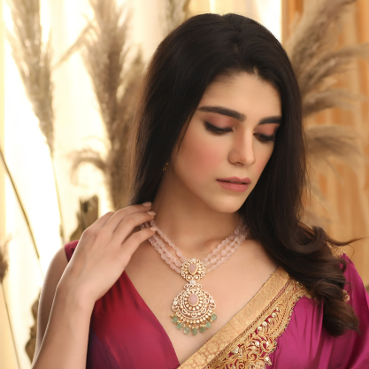 Woman wearing a pink saree with intricate gold detailing, showcasing an elegant traditional necklace with a detailed pendant.
